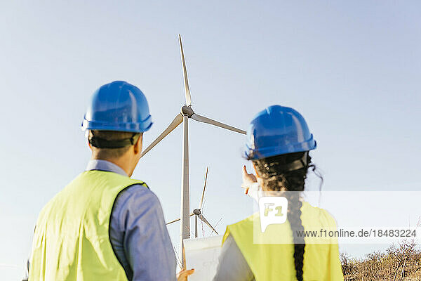 Engineer with colleague gesturing and discussing over wind turbines