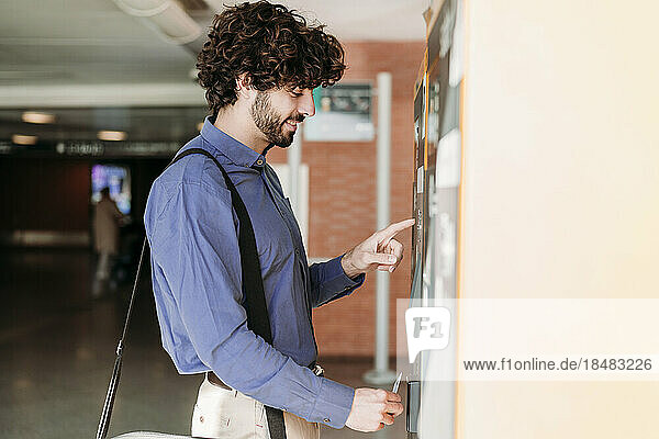 Happy young businessman with credit card using ticket machine