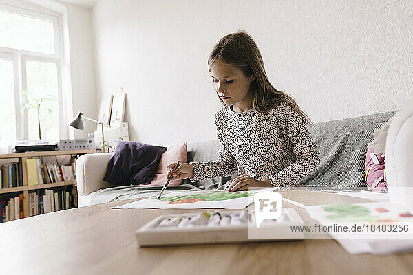 Mädchen malt zu Hause mit Pinsel auf Papier