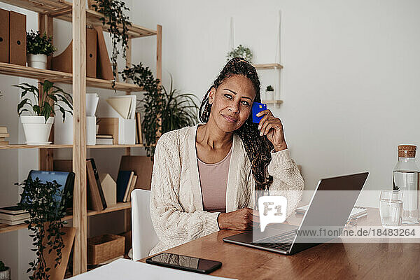 Thoughtful freelancer sitting with credit card and laptop at desk