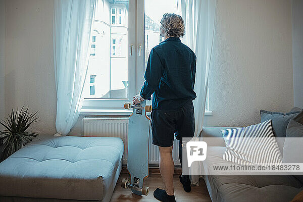 Man with skateboard looking through window at home