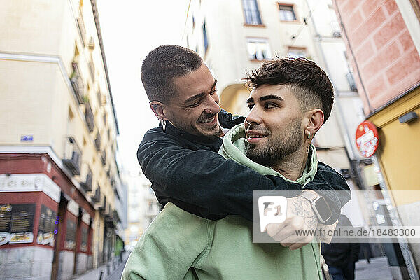 Happy gay man giving piggyback ride to boyfriend in city