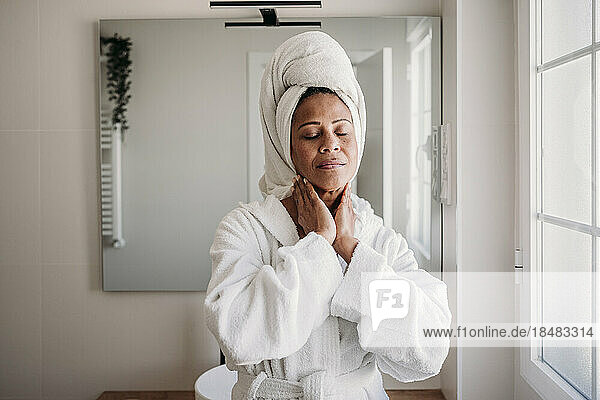 Smiling mature woman massaging face in bathroom at home