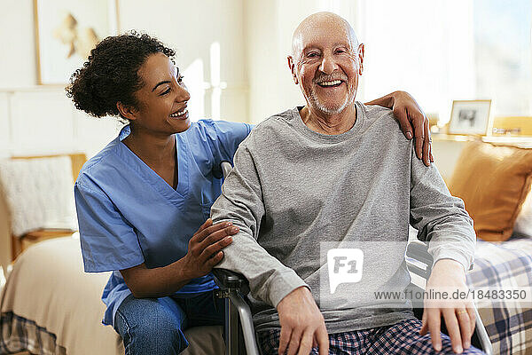 Glücklicher älterer Mann  der zu Hause von der Krankenschwester im Rollstuhl sitzt