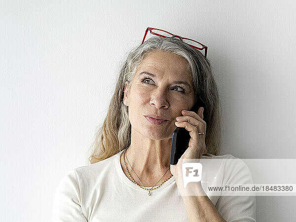 Thoughtful senior businesswoman talking on smart phone in front of wall