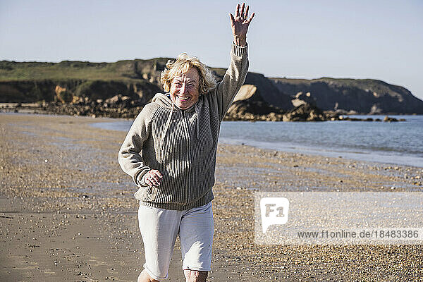 Fröhliche ältere Frau mit erhobenem Arm läuft am Strand