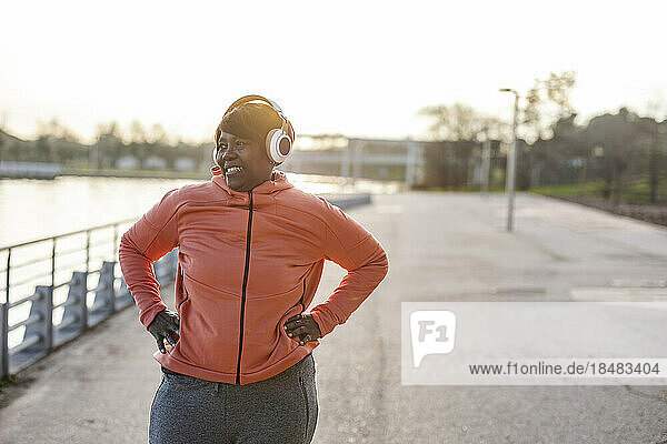 Smiling woman with wireless headphones exercising at promenade