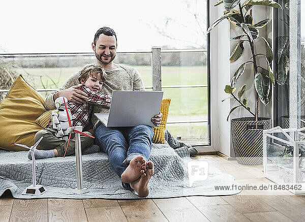 Father and son looking at laptop sitting on sofa with wind turbines