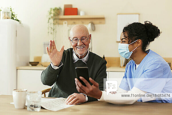 Smiling senior man waving on video call through smart phone at home