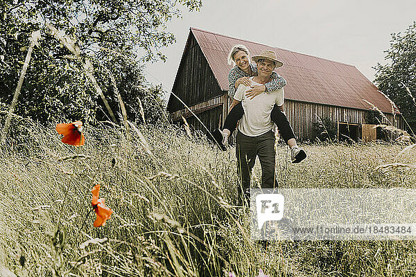 Happy man piggybacking woman in front of barn