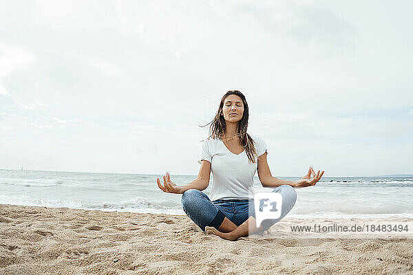 Woman practicing lotus position sitting cross-legged on sand at beach