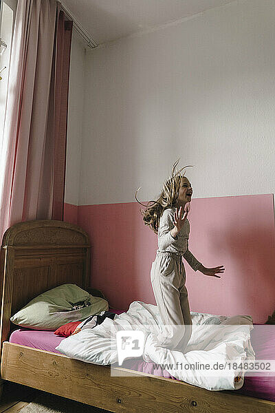 Fröhliches Mädchen  das Spaß beim Springen auf dem Bett im Schlafzimmer hat