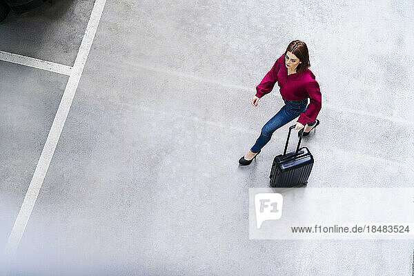 Businesswoman with wheeled luggage walking at parking lot