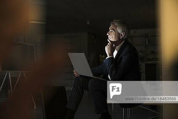 Thoughtful businessman with hand on chin sitting at office