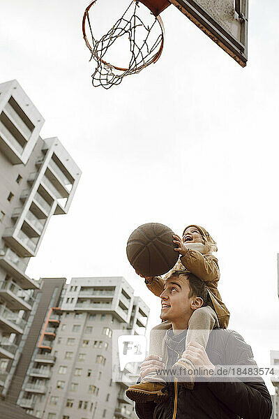 Father carrying daughter on shoulders and playing basketball
