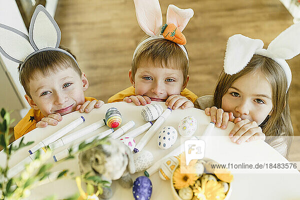 Smiling siblings wearing rabbit ears by table at home