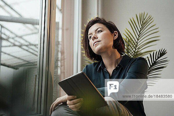 Contemplative young businesswoman with tablet PC in office