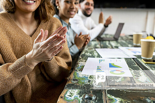 Business people applauding with charts on table in office
