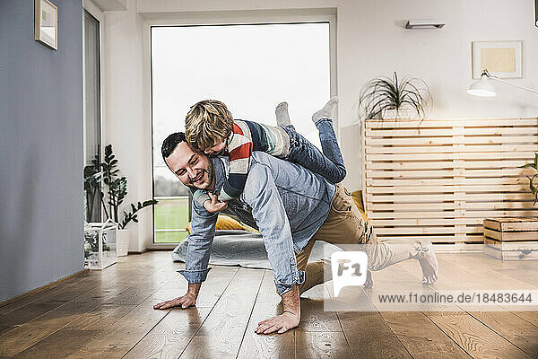 Boy balancing on back of father doing push-ups at home