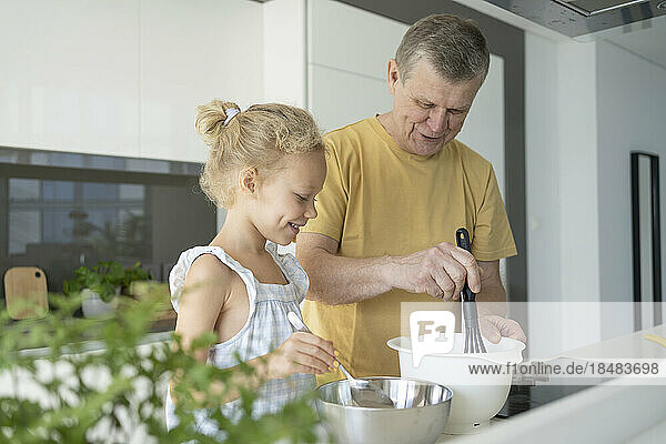 Grandfather and granddaughter preparing food in kitchen at home