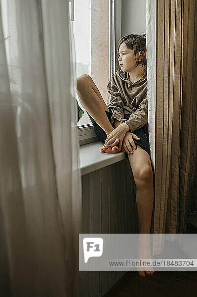 Thoughtful boy sitting on window sill
