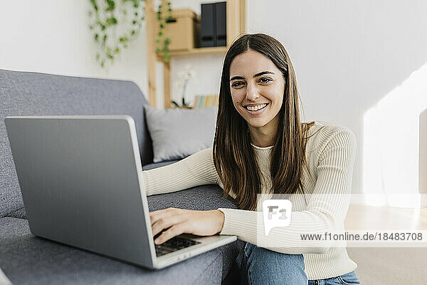 Smiling young woman sitting with laptop in living room