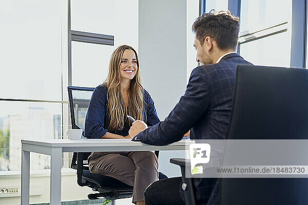 Smiling recruiter taking interview of candidate sitting at office