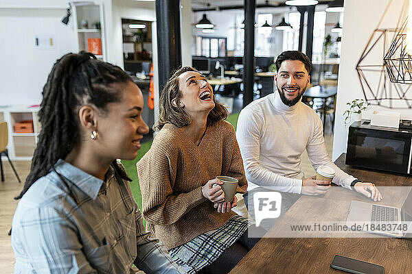 Geschäftsfrau lacht mit Kollegen in der Kaffeepause im Büro
