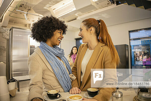 Cheerful young woman laughing with friend standing at cafe