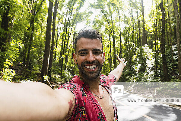 Fröhlicher Mann macht ein Selfie auf der Straße vor Bäumen
