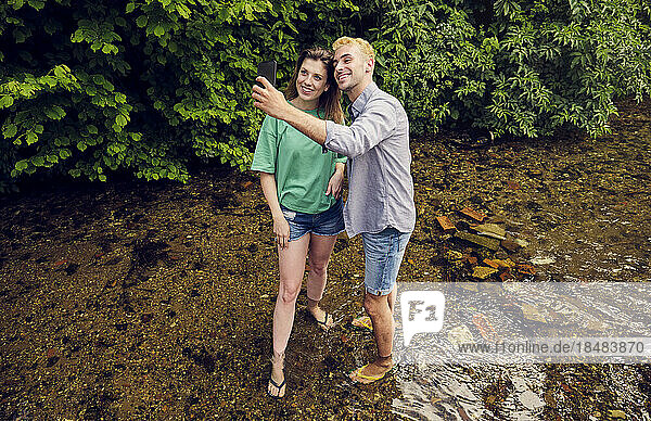 Young couple taking selfie through smart phone standing in stream