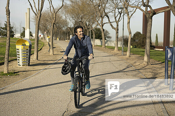 Glücklicher Mann fährt Fahrrad auf der Straße im Park