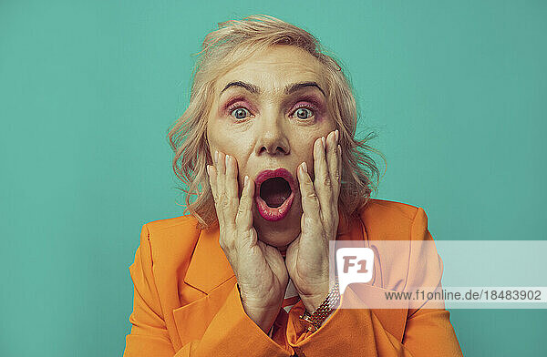 Shocked senior woman against turquoise background