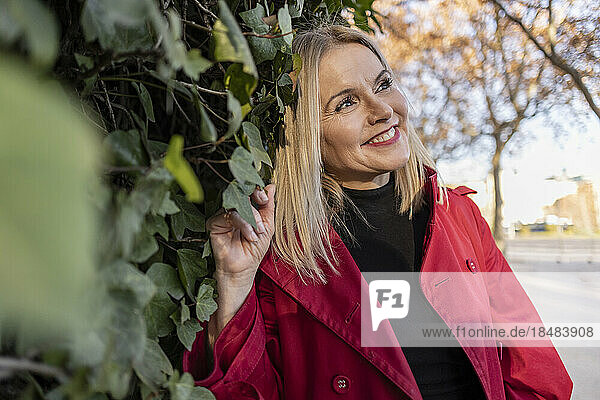 Thoughtful smiling mature woman leaning on plants