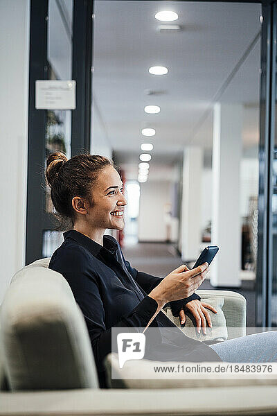 Happy businesswoman sitting with mobile phone in office