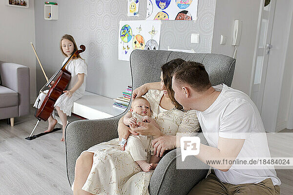 Parents holding baby boy with girl playing musical instrument in background