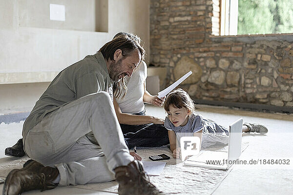 Mature man and woman reading documents with daughter lying on rug at home