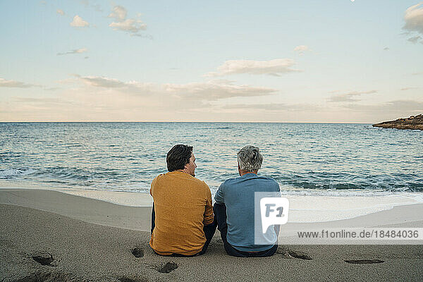 Mann und Vater sitzen bei Sonnenuntergang zusammen am Strand