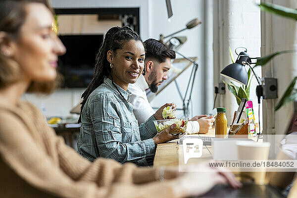 Lächelnde Geschäftsfrau  die im Büro Salat isst