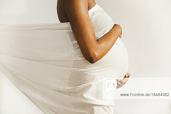 Pregnant woman covered in white sheet in front of wall
