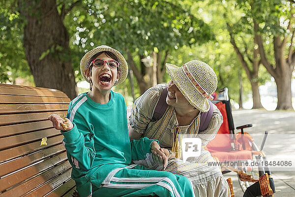 Cheerful girl with disability having fun with mother sitting on bench