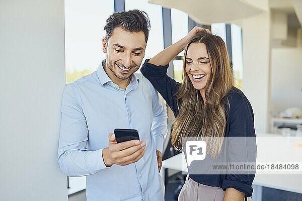 Zufriedene Geschäftskollegen schauen sich ihr Smartphone an und genießen es am Arbeitsplatz