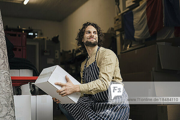 Lächelnder junger Geschäftsmann trägt Karton im Lagerraum