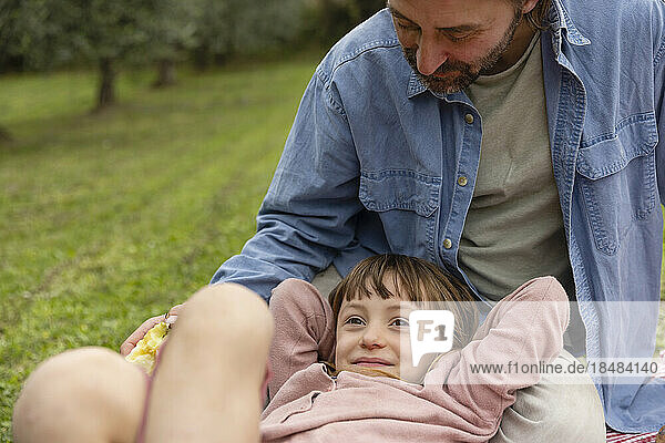 Smiling girl relaxing with father sitting on field