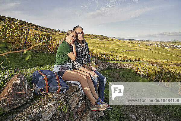 Smiling thoughtful couple sitting on wall in vineyard