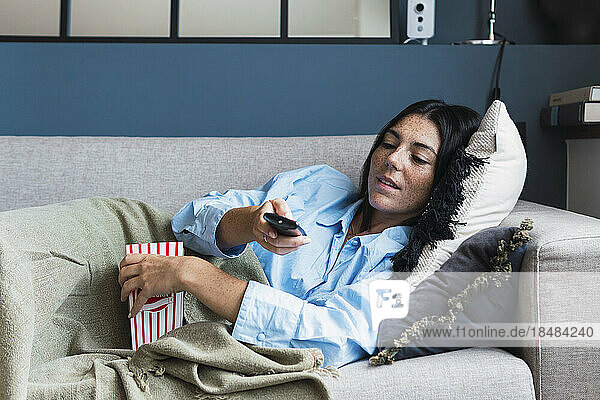 Junge Frau mit TV-Fernbedienung ruht auf Sofa im Wohnzimmer