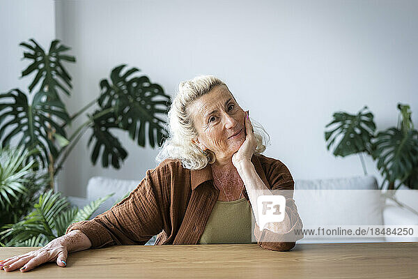 Lächelnde ältere Frau  die sich zu Hause auf den Ellenbogen stützt