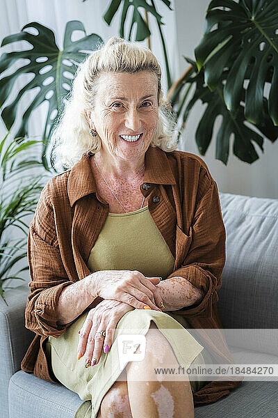 Fröhliche ältere Frau sitzt zu Hause auf dem Sofa