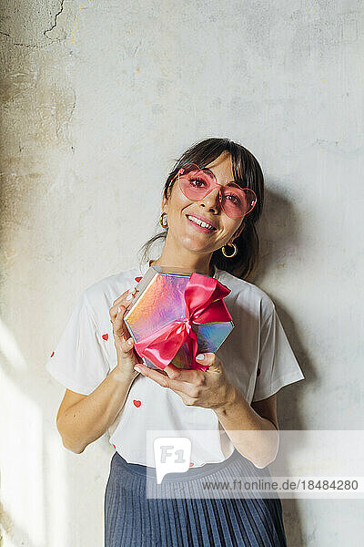 Smiling woman wearing eyeglasses standing with gift box