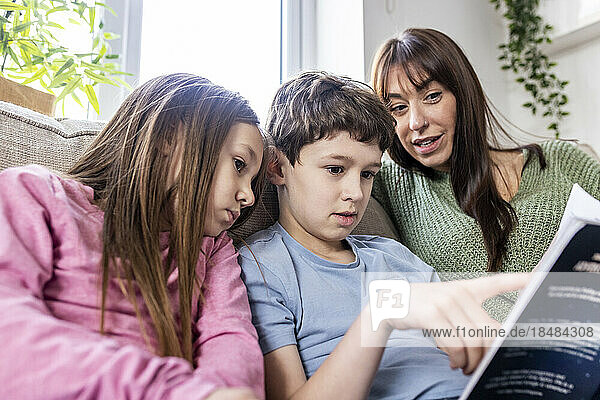 Boy reading book with sister and mother at home